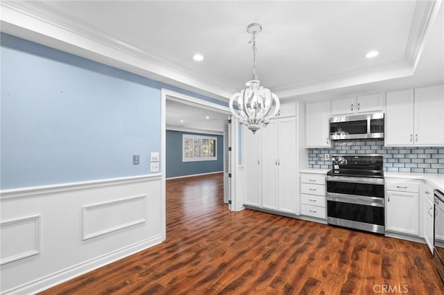 kitchen featuring wainscoting, a tray ceiling, stainless steel appliances, crown molding, and light countertops