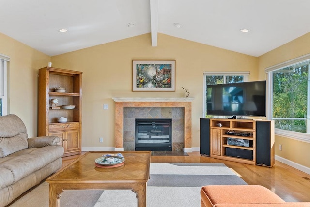 living room featuring vaulted ceiling with beams, light hardwood / wood-style floors, and a tile fireplace