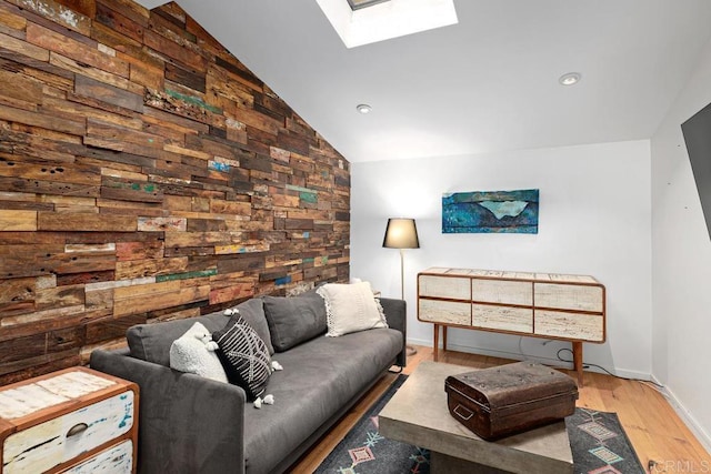 living room featuring wooden walls, light hardwood / wood-style floors, and vaulted ceiling with skylight