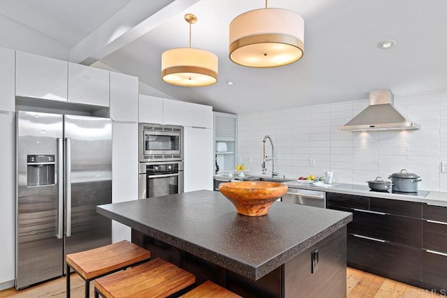 kitchen with range hood, tasteful backsplash, white cabinetry, decorative light fixtures, and stainless steel appliances