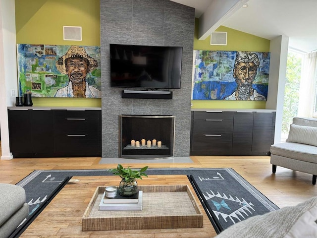 living room with a tiled fireplace, lofted ceiling with beams, and light wood-type flooring