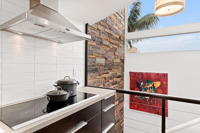 kitchen with dark brown cabinetry, backsplash, exhaust hood, and black electric stovetop