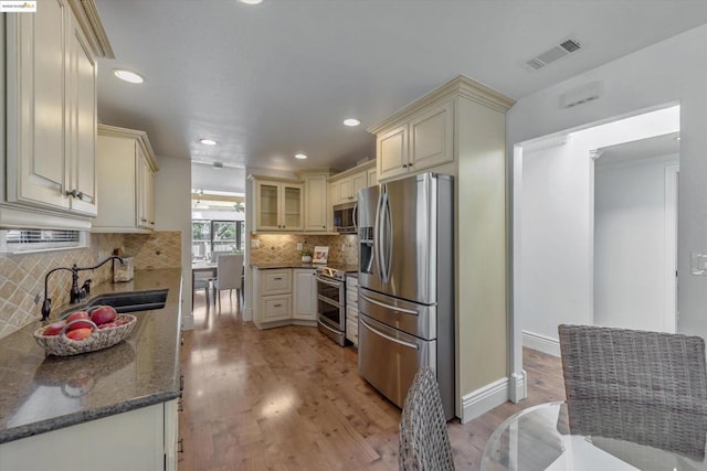 kitchen featuring sink, dark stone countertops, appliances with stainless steel finishes, light hardwood / wood-style floors, and cream cabinetry