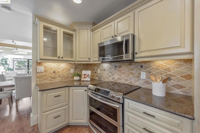 kitchen featuring light hardwood / wood-style flooring, dark stone counters, stainless steel appliances, cream cabinets, and decorative backsplash