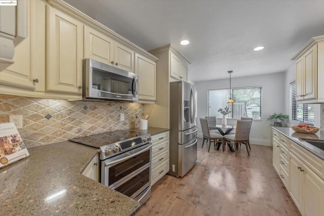 kitchen featuring light stone counters, cream cabinets, pendant lighting, and stainless steel appliances