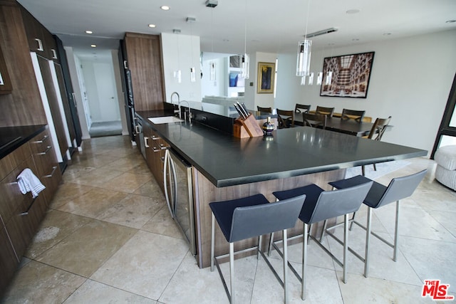 kitchen with sink, hanging light fixtures, a kitchen breakfast bar, dark brown cabinetry, and a center island with sink