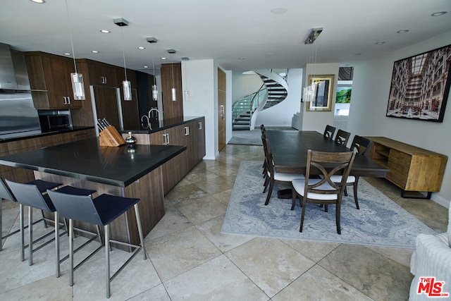 kitchen featuring an island with sink, a breakfast bar, pendant lighting, and dark brown cabinetry