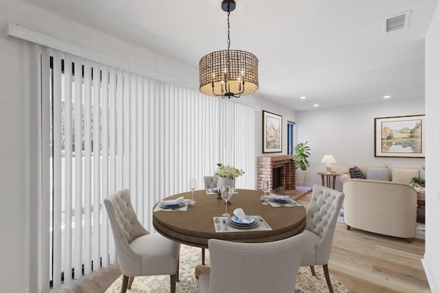 dining area featuring an inviting chandelier, a fireplace, and light wood-type flooring