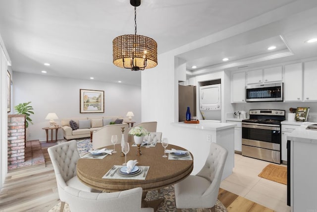 dining area featuring stacked washer and clothes dryer, a tray ceiling, a chandelier, and light hardwood / wood-style floors