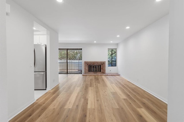 unfurnished living room with a brick fireplace and light hardwood / wood-style flooring