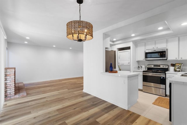 kitchen featuring appliances with stainless steel finishes, pendant lighting, white cabinets, stacked washer and dryer, and kitchen peninsula