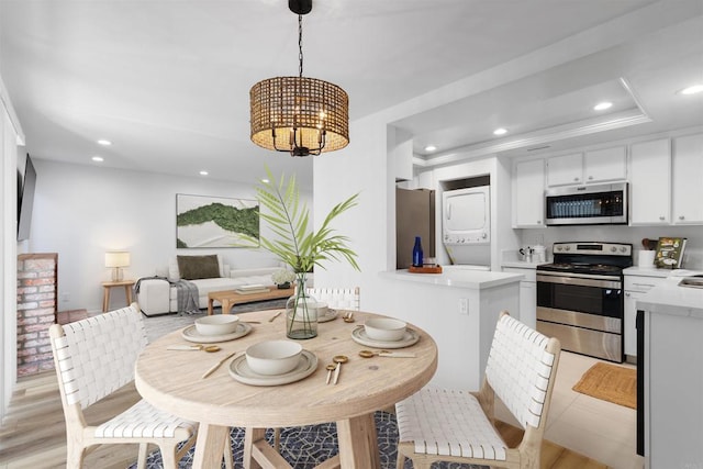 dining space with light wood finished floors, an inviting chandelier, a tray ceiling, recessed lighting, and stacked washer / drying machine