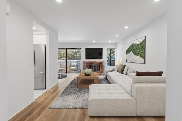 living area with recessed lighting, a brick fireplace, baseboards, and light wood-style floors