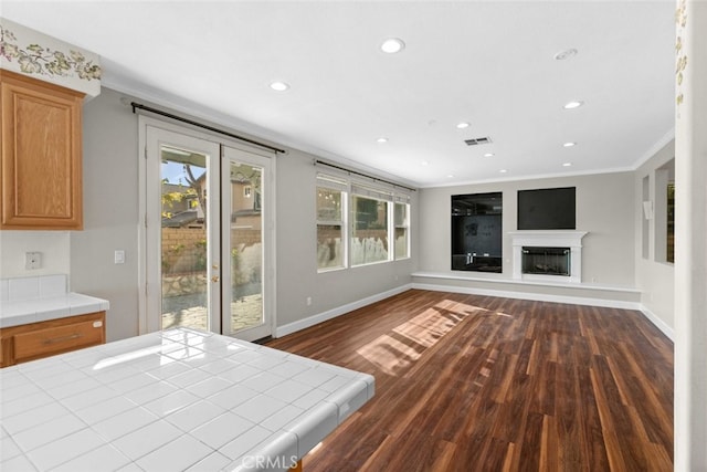 interior space with visible vents, a glass covered fireplace, ornamental molding, dark wood-style flooring, and access to outside