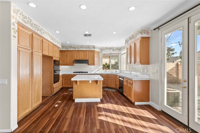 kitchen with under cabinet range hood, gas stovetop, visible vents, light countertops, and a center island