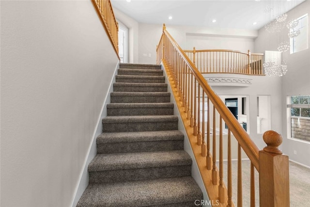 staircase with a towering ceiling, a chandelier, and carpet floors