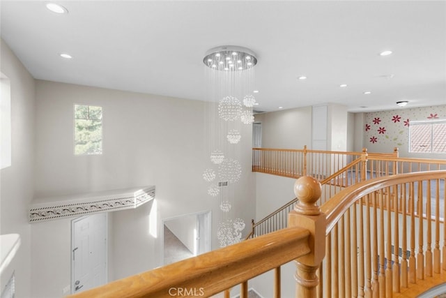 corridor featuring recessed lighting, a chandelier, a wealth of natural light, and an upstairs landing