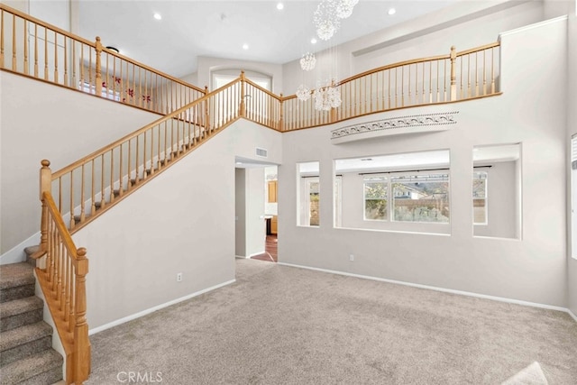 unfurnished living room featuring a chandelier, recessed lighting, carpet flooring, a towering ceiling, and baseboards