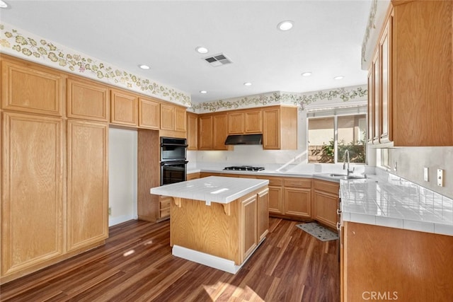 kitchen featuring tile counters, visible vents, dobule oven black, a sink, and under cabinet range hood