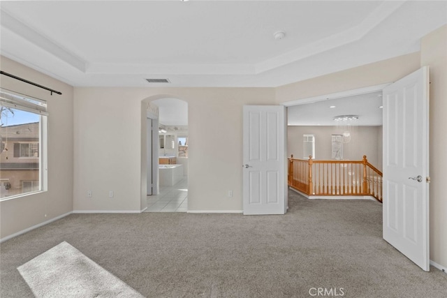 unfurnished room with visible vents, arched walkways, a raised ceiling, baseboards, and carpet