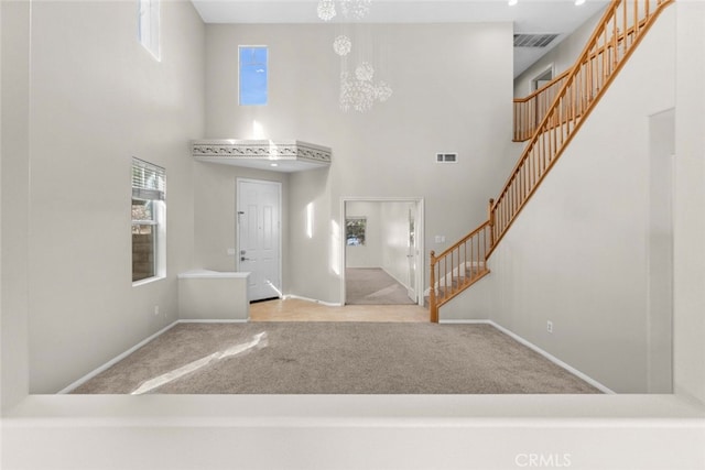 carpeted foyer entrance with visible vents, a notable chandelier, stairway, and a towering ceiling