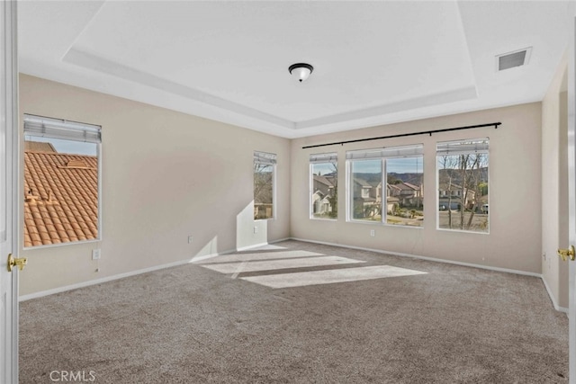 unfurnished room featuring carpet floors, a tray ceiling, visible vents, and baseboards