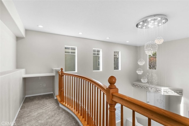 corridor featuring baseboards, carpet flooring, an upstairs landing, and an inviting chandelier