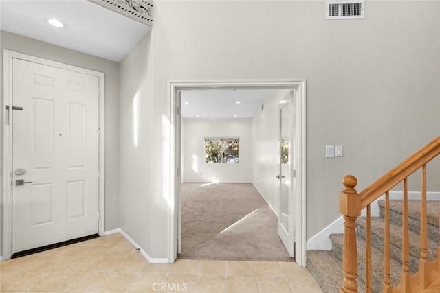 foyer with light tile patterned floors, visible vents, stairway, light carpet, and baseboards