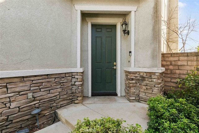 property entrance with stone siding, fence, and stucco siding