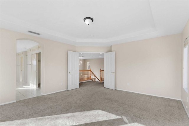 carpeted empty room featuring arched walkways, a raised ceiling, visible vents, and baseboards