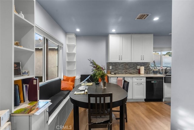 kitchen with white cabinets, decorative backsplash, light hardwood / wood-style flooring, and black dishwasher