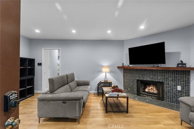 living room with a tiled fireplace and light wood-type flooring