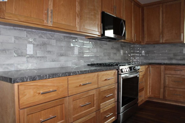 kitchen with tasteful backsplash, appliances with stainless steel finishes, dark hardwood / wood-style floors, and dark stone counters