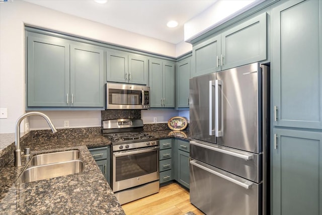 kitchen featuring stainless steel appliances, sink, dark stone countertops, and light hardwood / wood-style flooring