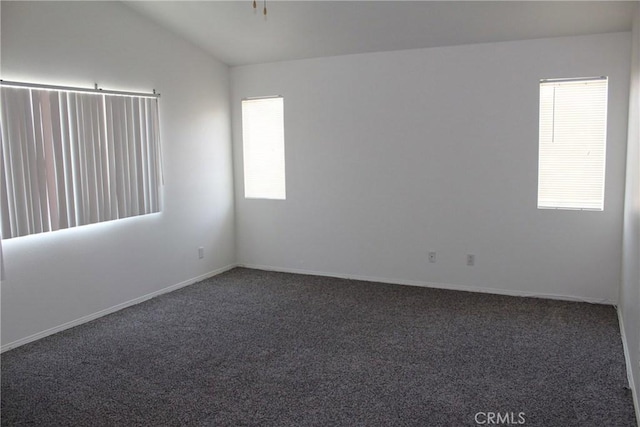 unfurnished room with a healthy amount of sunlight, vaulted ceiling, and dark colored carpet