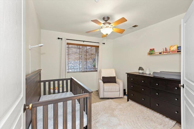 bedroom featuring a nursery area, light colored carpet, visible vents, and ceiling fan