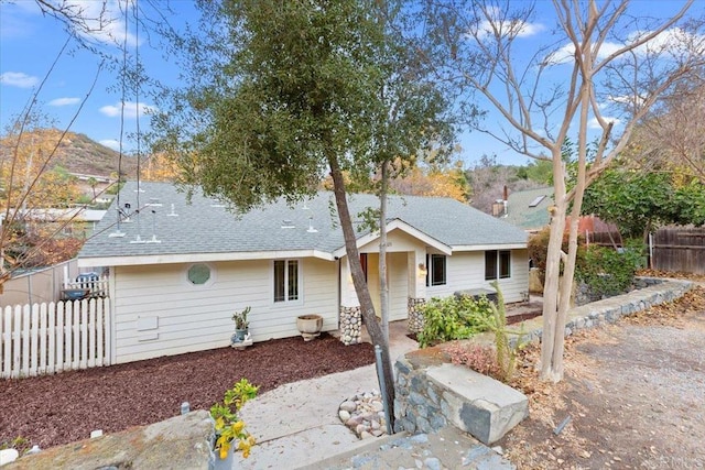 ranch-style house featuring roof with shingles and fence