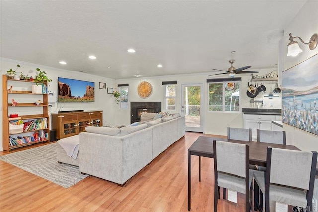 living area with a glass covered fireplace, crown molding, recessed lighting, and light wood-style floors