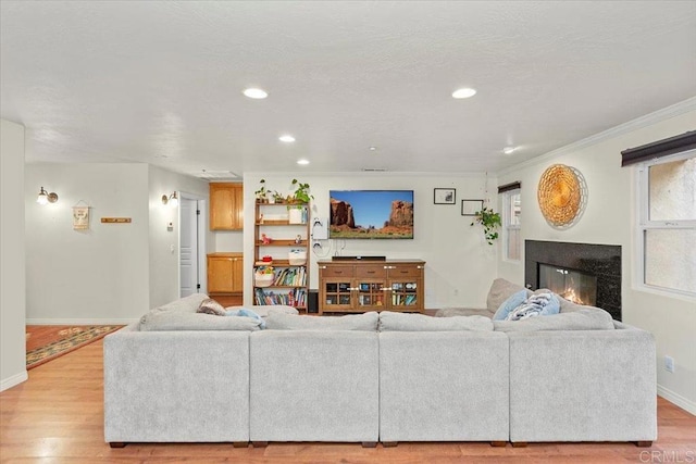 living room featuring recessed lighting, light wood-style flooring, baseboards, and a glass covered fireplace