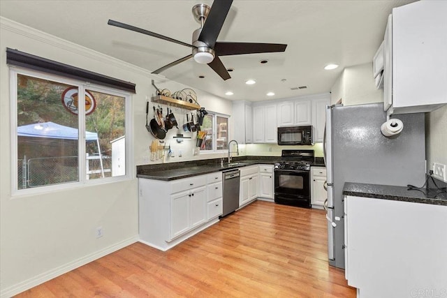 kitchen featuring light wood-type flooring, dark countertops, black appliances, and white cabinetry