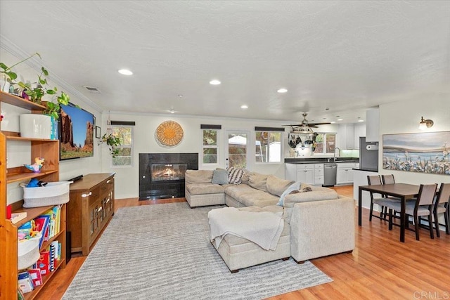 living area with light wood-style floors, visible vents, a high end fireplace, and a healthy amount of sunlight