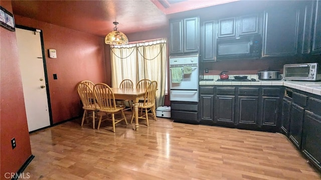 kitchen with decorative light fixtures, tile countertops, black appliances, and light hardwood / wood-style floors