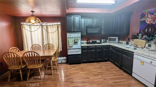 kitchen with decorative light fixtures, tile counters, white appliances, a textured ceiling, and light hardwood / wood-style flooring