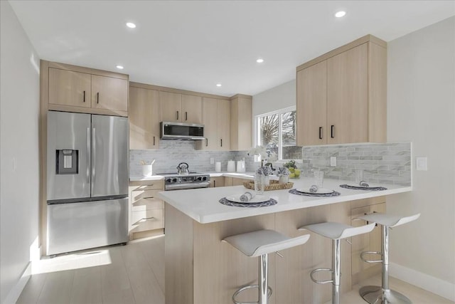 kitchen featuring appliances with stainless steel finishes, a kitchen breakfast bar, decorative backsplash, kitchen peninsula, and light brown cabinets