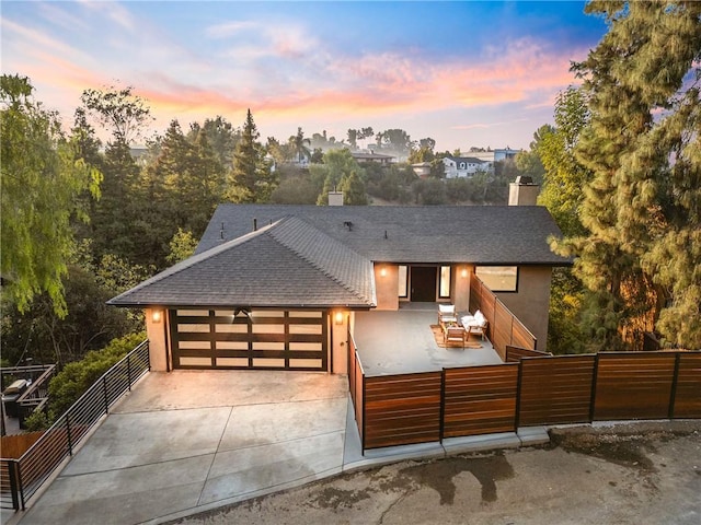 view of front facade with roof with shingles, an attached garage, stucco siding, concrete driveway, and fence private yard