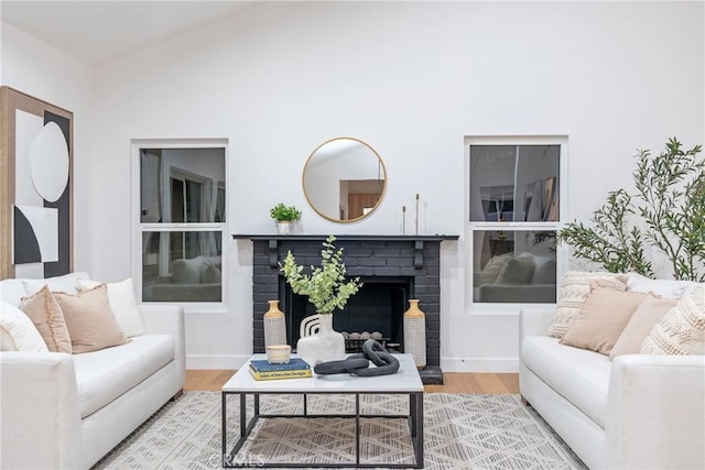 living area with baseboards, wood finished floors, a fireplace, and vaulted ceiling