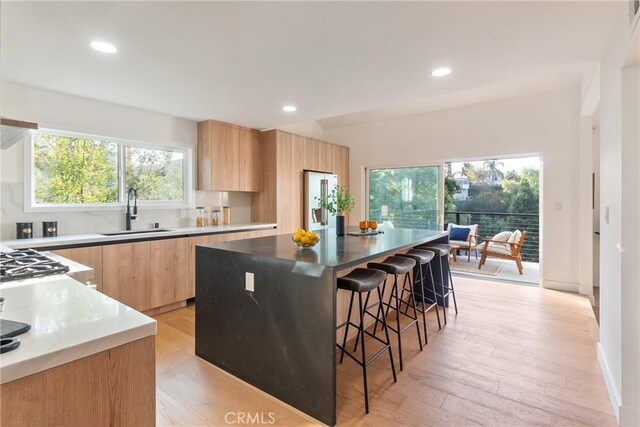 kitchen with a breakfast bar area, light brown cabinetry, a sink, modern cabinets, and a center island