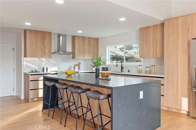 kitchen with wall chimney exhaust hood, modern cabinets, light brown cabinetry, and a sink