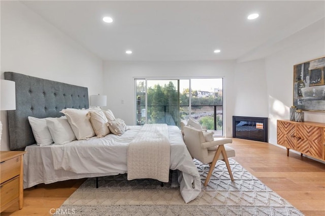 bedroom with a glass covered fireplace, light wood-style flooring, and recessed lighting