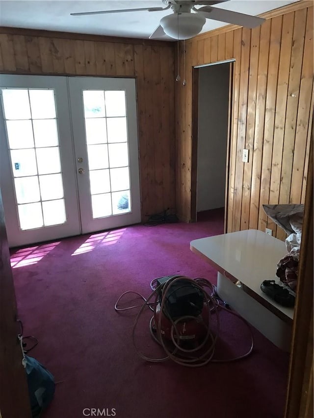 interior space with wooden walls, french doors, ceiling fan, and carpet